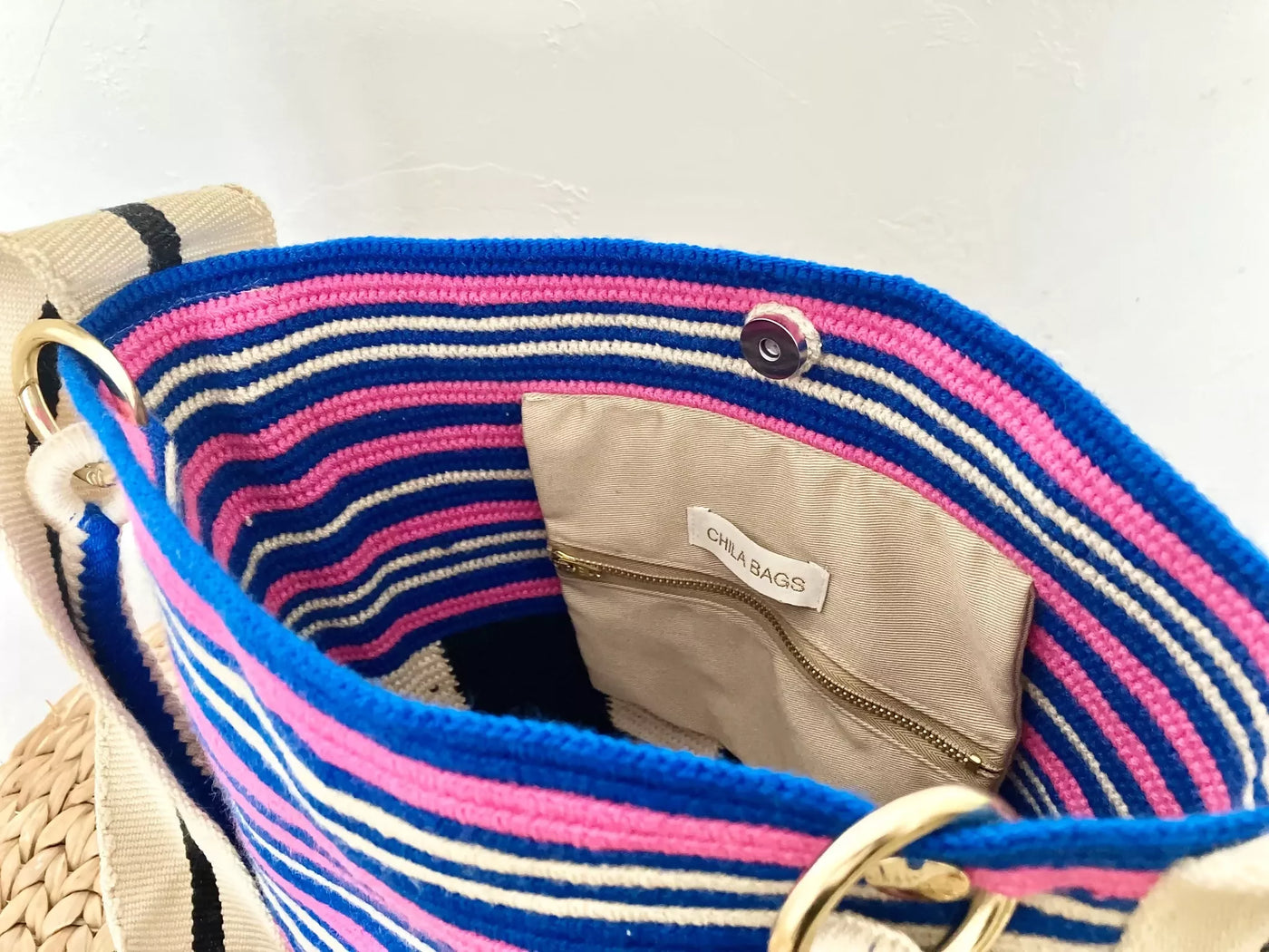 ハラカドのコロンビア発 Arequipe Bag Blue は、明るいブルー、ピンク、ホワイトのストライプが特徴のカラフルな織りバッグです。内側にはベージュの生地の裏地があり、ジッパー付きポケットが付いています。このサステナブルなアクセサリーには、金属リングと磁気スナップ留めが含まれており、内側には「CHA BAGS」と書かれたラベルが付いています。アクリル100%で作られており、スタイルと機能性を兼ね備えています。